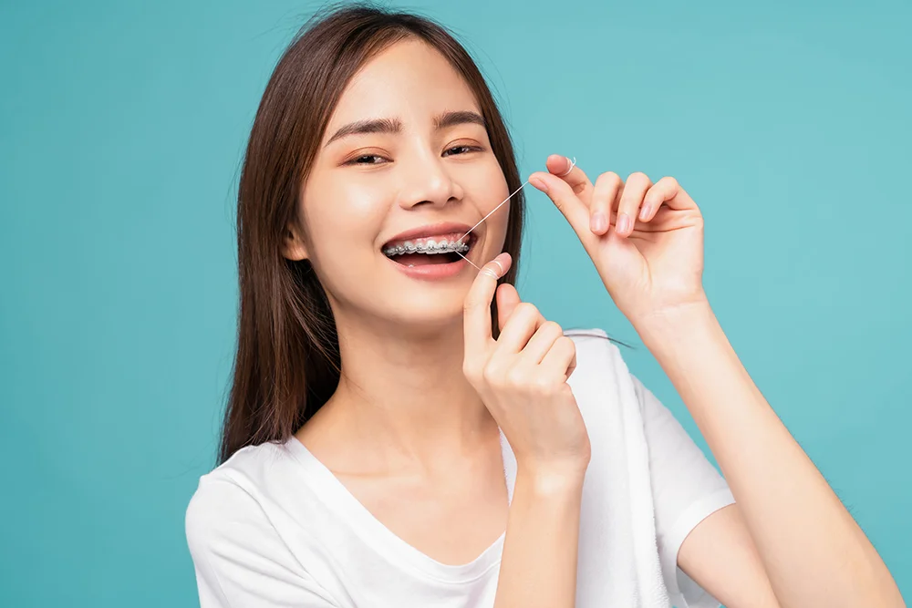 Young Asian woman cleaning braces on teeth with dental floss on blue background, Concept oral hygiene and health care.