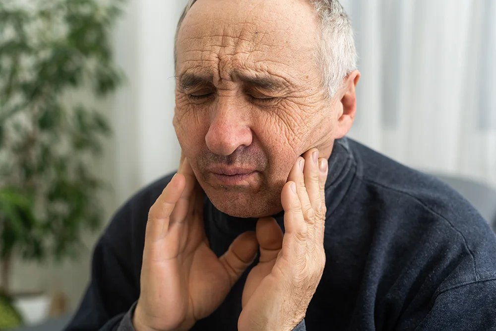 Old man with toothaches. Elderly senior man has toothaches. Unhappy man face in tooth pain sitting on sofa at home, feel sick unwell. Sad aged man hand holding his chin. Adult suffering toothache