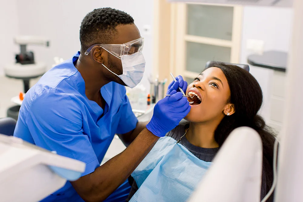Close-up portrait of the African young woman patient examining by male dentist with tools in dental clinic. Emergency care