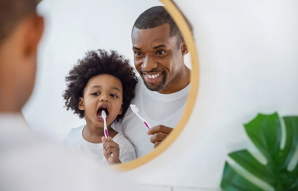 Portrait of happy family black African American father and son child boy brushing teeth in the bathroom. Morning routine with toothbrushes, father’s day concept