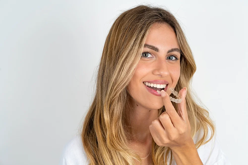 Young beautiful caucasian woman over white background holding an invisible aligner ready to use it. Dental healthcare and confidence concept.