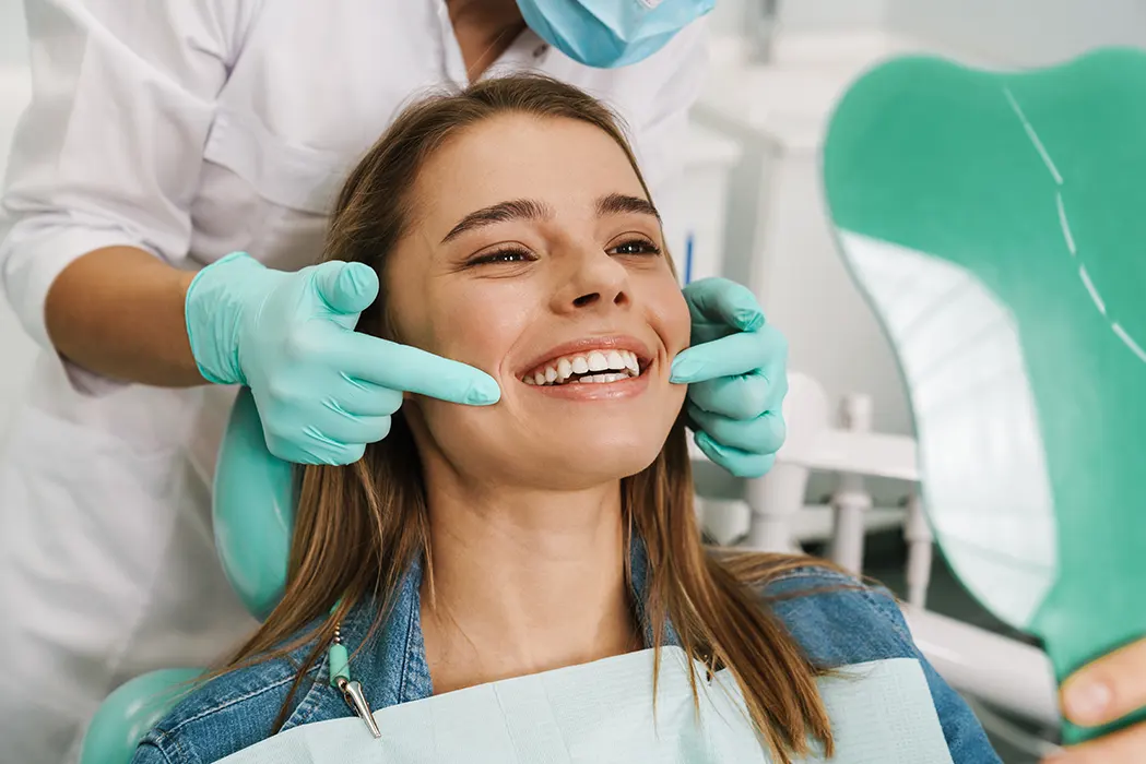 European young woman smiling while looking at mirror in dental clinic. Maxillofacial Surgery